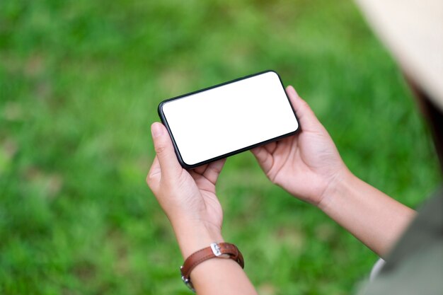 Mockup-afbeelding van een vrouw met een zwarte mobiele telefoon met een leeg desktopscherm in het park