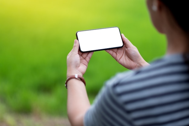 Mockup-afbeelding van een vrouw met een zwarte mobiele telefoon met een leeg desktopscherm met een wazige groene natuurachtergrond