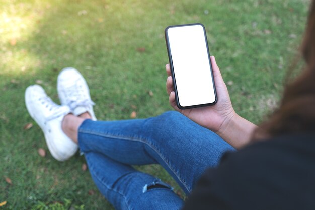 Mockup-afbeelding van een vrouw met een zwarte mobiele telefoon met een leeg wit scherm terwijl ze in de buitenlucht zit