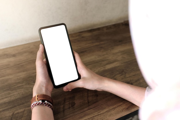 Foto mockup-afbeelding van een vrouw met mobiele telefoon met leeg scherm op houten tafel