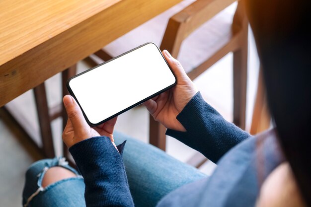 Mockup-afbeelding van een vrouw met zwarte mobiele telefoon met een leeg wit scherm in café