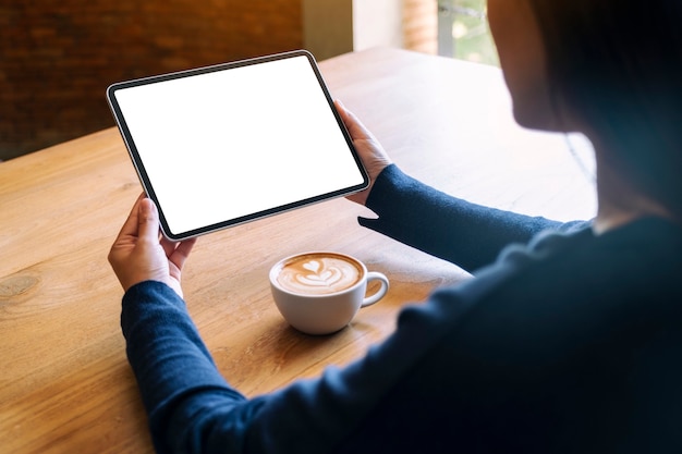 Mockup afbeelding van een vrouw met zwarte tablet pc met leeg wit scherm met koffiekopje op houten tafel