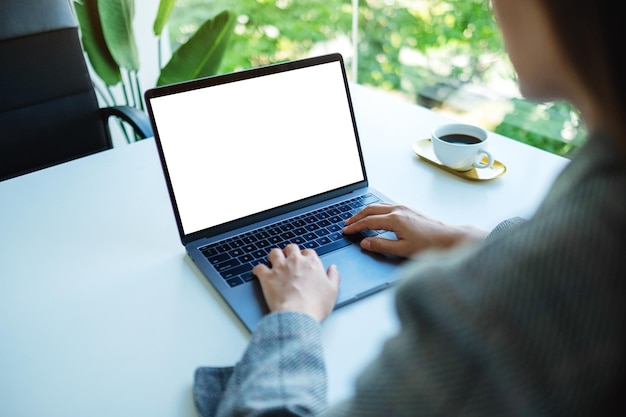 Mockup-afbeelding van een zakenvrouw die op het toetsenbord van de laptop met een leeg wit desktopscherm op kantoor typt en gebruikt