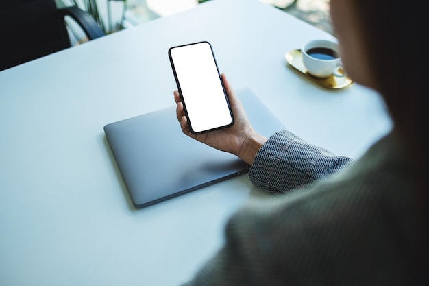 Mockup-afbeelding van een zakenvrouw met een mobiele telefoon met een leeg wit desktopscherm met een laptop op tafel