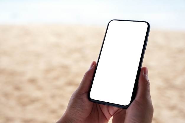 Mockup-afbeelding van handen met zwarte mobiele telefoon met leeg desktopscherm aan zee