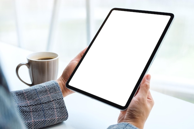 Mockup-afbeelding van handen met zwarte tablet-pc met leeg wit scherm met koffiekopje op tafel