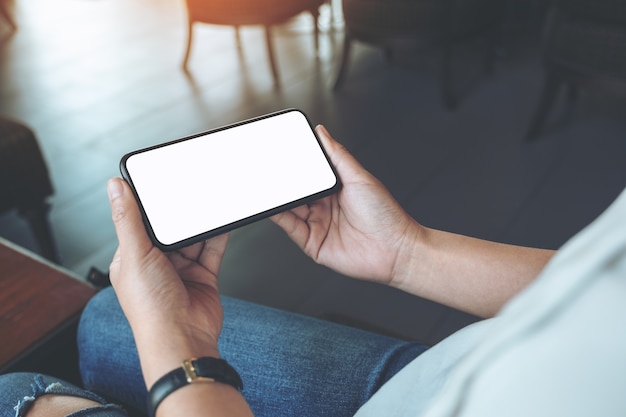 Mockup afbeelding van vrouw handen met zwarte mobiele telefoon met leeg wit scherm horizontaal in café