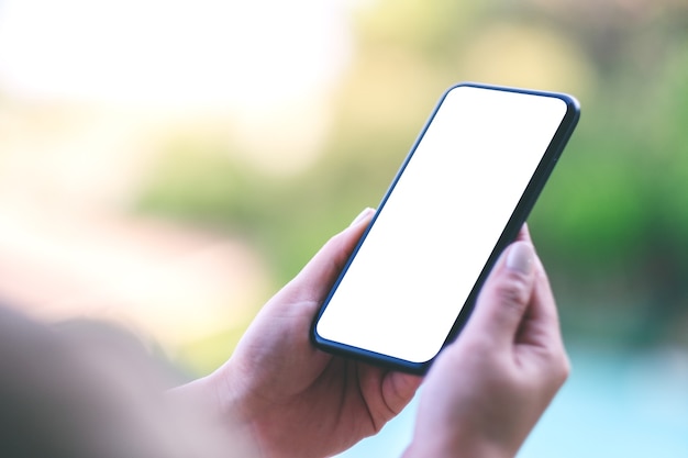 Mockup afbeelding van vrouw handen met zwarte mobiele telefoon met leeg wit scherm met wazig aard achtergrond