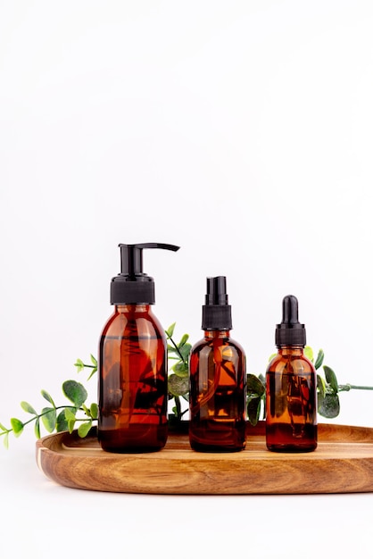 Mockup of amber glass bottles with serum jars of hand cream faces on wooden stand isolated on white backgroundxA