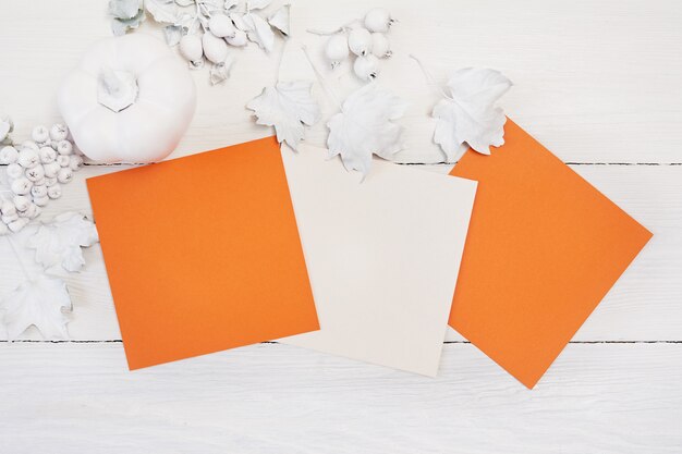 Mockup autumn. two orange sheets of paper, white pumpkin, berries and leaves.