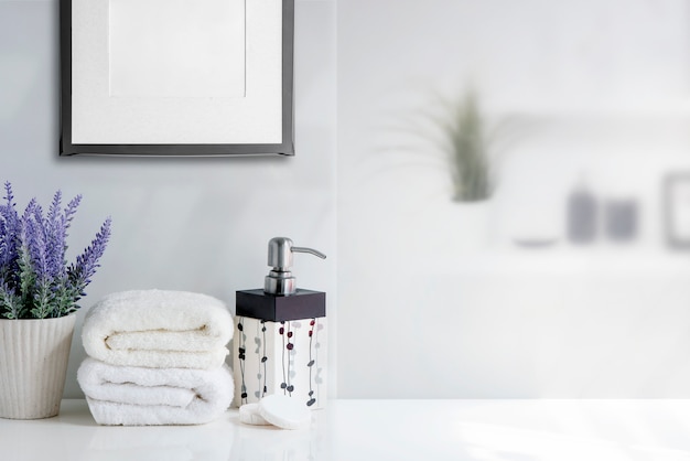 Фото Полотенце ванны модель-макета с бутылкой жидкого мыла и комнатное растение на белой таблице в белой комнате.