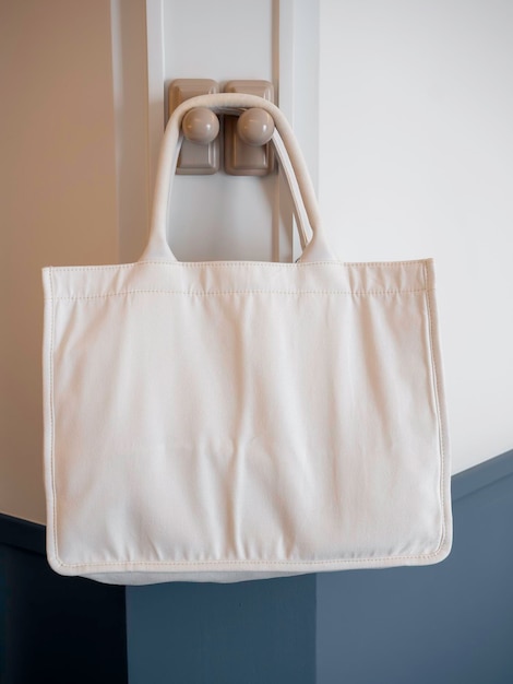 Mockup big tote bag hanging on the white wall in the room vertical style Eco Friendly empty white color fashion canvas tote bag Reusable fabric container for shopping Design template mockup