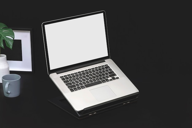 Mockup blank screen laptop computer, mug, ceramic vase and wooden picture frame on black background.