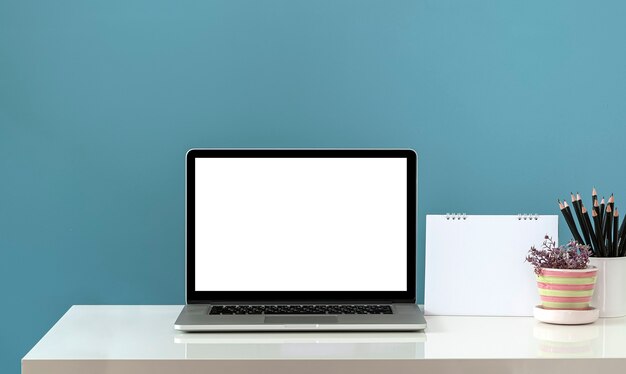 Mockup blank screen laptop computer and supplies on white table\
and light blue wall background.