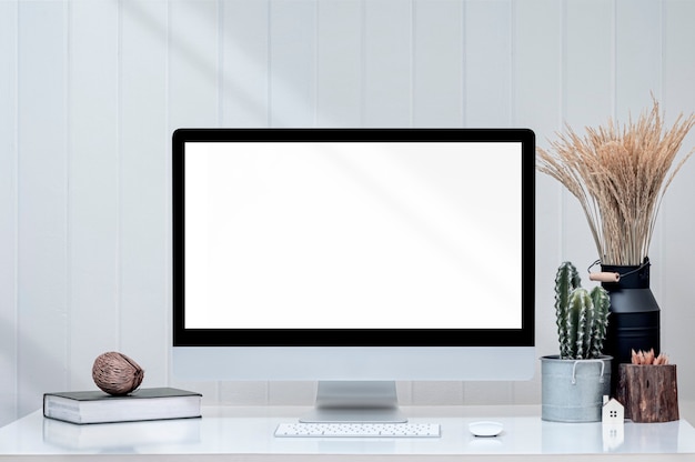 Mockup blank screen monitior with supplies on white top table and white wooden wall