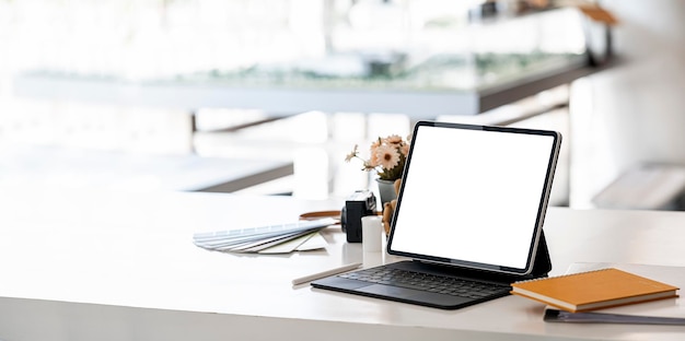 Mockup blank screen portable tablet with magic keyboard on white table in modern office room.