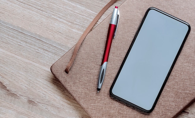 ペンとテーブルの上の日記とモックアップの空白の画面のスマートフォン。