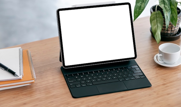 Mockup blank screen tablet, coffee cup and notebook on wooden table.