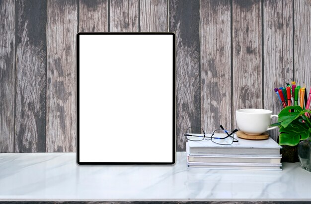 Mockup blank screen tablet and supplies on marble table with old wooden wall.