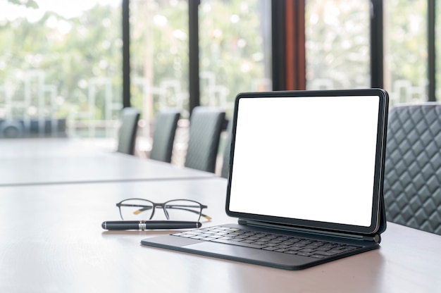 Mockup blank screen tablet with magic keyboard on wooden table in meeting room.