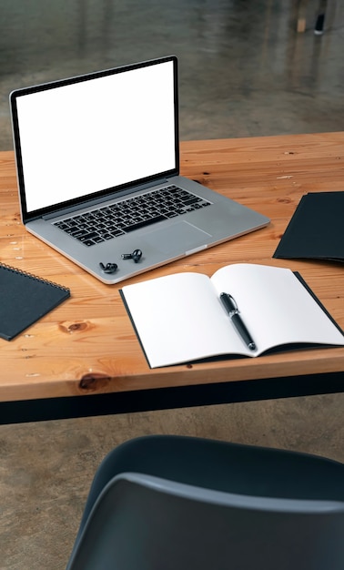 Mockup blank white screen laptop computer and supplies on wooden table, vertical view.