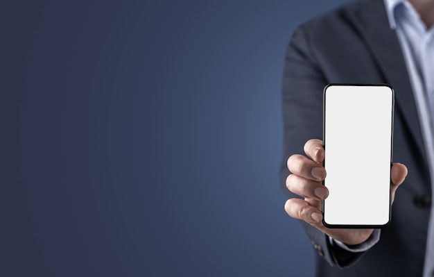 Макет мобильного телефона бизнесмена в костюме, показывающего пустой белый экран мобильного телефона в горизонтальном положении на синем фоне