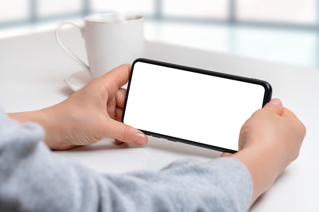 Mockup cellphone horizontal position mockup image of woman\
holding black mobile phone with blank screen with coffee cup on\
table closeup of woman hand holding smartphone horizontal\
position