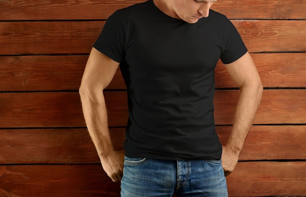 Mockup clothes. Athletic fit guy in a black T-shirt and blue jeans on a brown wooden studio background. Template ready for you design