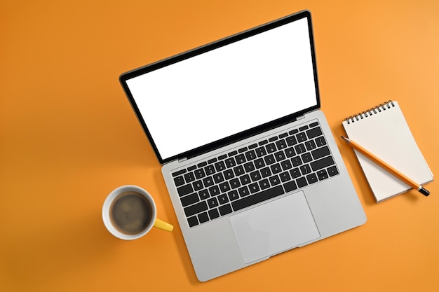 Photo mockup computer laptop with empty scree coffee cup and notepad on yellow background top view