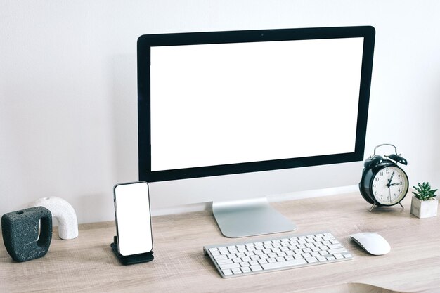 Photo mockup of computer and mobile phone with white blank screen on office table