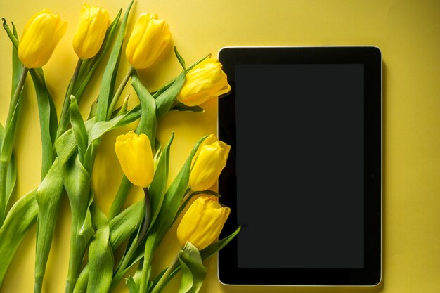 Mockup computer tablet with bouquet of tulips on top view on colorful yellow background panoramic shot