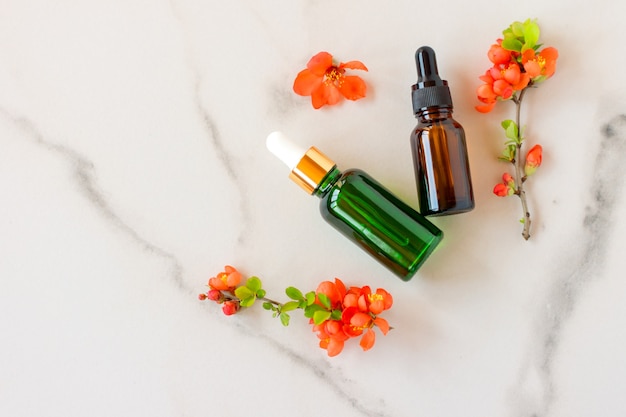 Mockup cosmetic face serum brown glass bottle with a pipette on a marble background with orange flowers. Female beauty concept, empty template. Copy space.