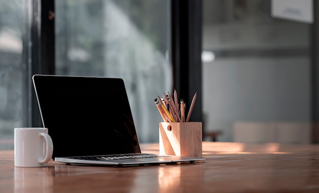 검은 화면 노트북 컴퓨터, 찻잔 및 현대 사무실 방에 나무 테이블에 연필의 나무 상자 모형 창조적 인 작업 공간.
