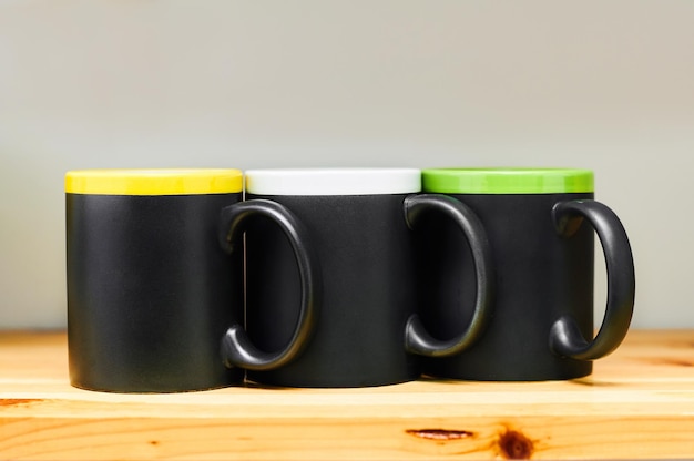 Photo mockup for design on black cups or mugs on light wooden shelf dishes in kitchen place for text