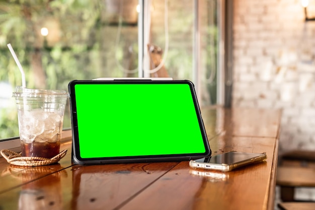 コーヒーとスマートフォンと空の画面でデジタルタブレットのモックアップは、背景の白い画面のようにコーヒーショップの木製のオフィスの机に分離します