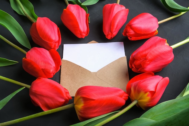 Mockup of fresh red tulips bouquet and greeting card in kraft envelope 