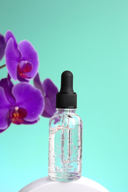 Mockup of glass bottle on green background Purple orchid flowers are located next to bubble with oil Concept of skin care spa treatments natural cosmetics