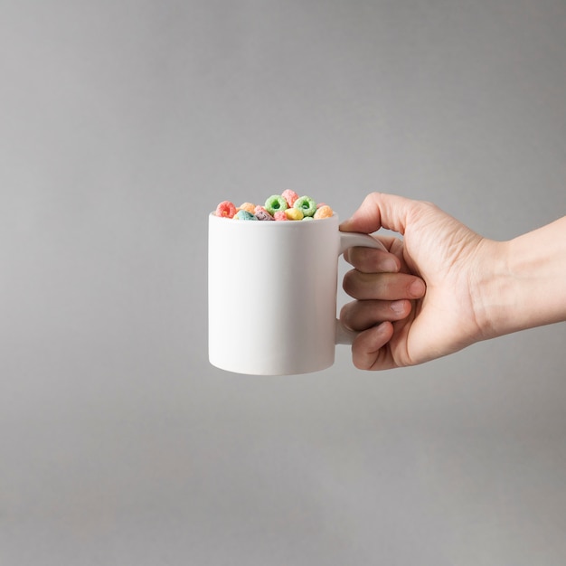 Mockup of hand holding mug of colorful cereals