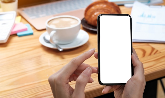 Mockup image blank white screen cell phone.women hand holding texting using mobile on desk at home office.