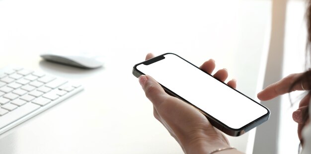 Макет изображения пустой белый экран сотовый телефон. женская рука текстовых сообщений с помощью мобильного телефона на столе в домашнем офисе.
