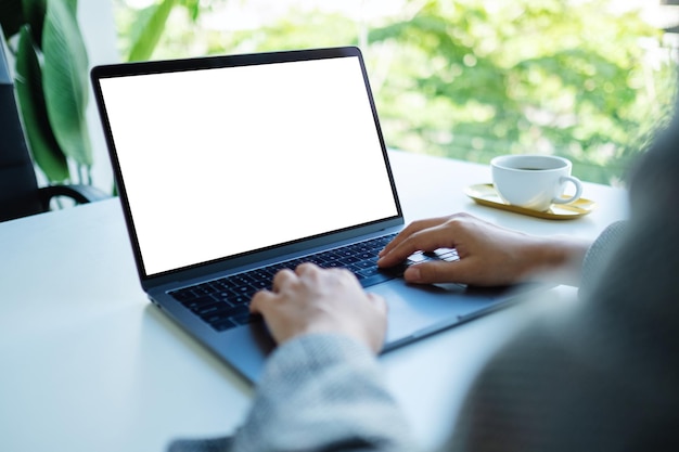 Mockup image of a businesswoman using and typing on laptop keyboard with blank white desktop screen in the office