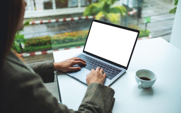 Immagine mockup di una donna d'affari che utilizza e digita sulla tastiera del laptop con schermo desktop bianco vuoto in ufficio