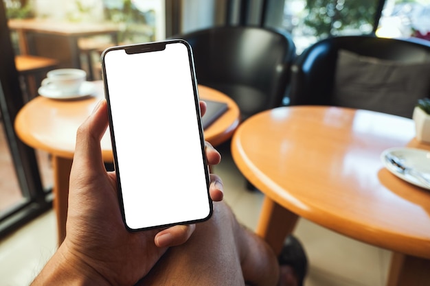 Mockup image of a hand holding and showing mobile phone with blank white screen in cafe