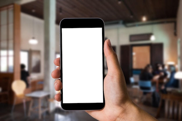 Mockup image of hand holding white mobile phone with blank\
white screen in cafe