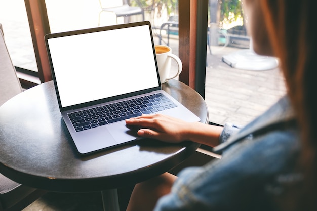 Mockup image of a hand using and touching on laptop touchpad with blank white desktop screen with coffee cup on the table