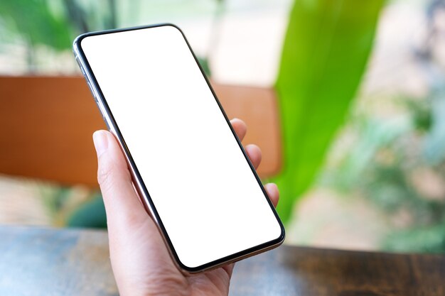 Mockup image of hands holding black mobile phone with blank desktop screen with green nature background