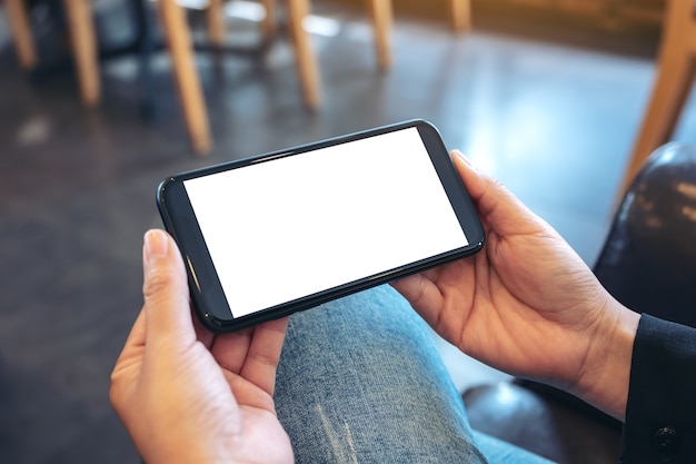 Макет изображения рук, держащих черный мобильный телефон с пустым белым экраном