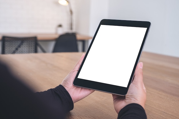 Mockup image of hands holding and looking at black tablet pc with blank white screen while sitting in office