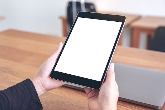 Mockup image of hands holding and using black tablet pc with blank white desktop screen