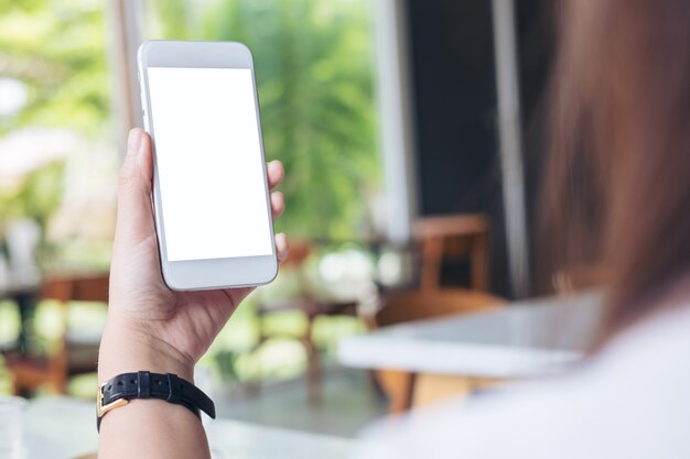 Mockup image of hands holding white mobile phone with blank white screen in modern cafe